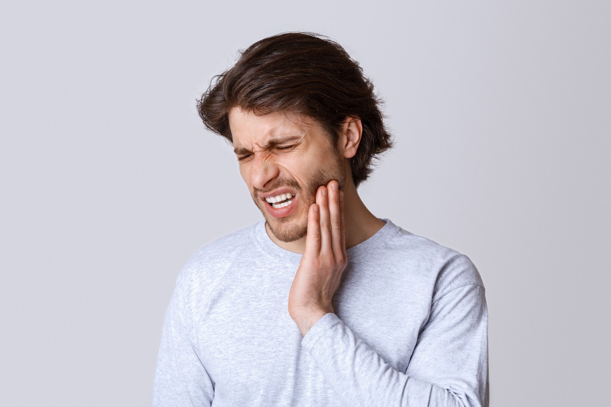 Man touching cheek in pain against white background, expressing dental discomfort.