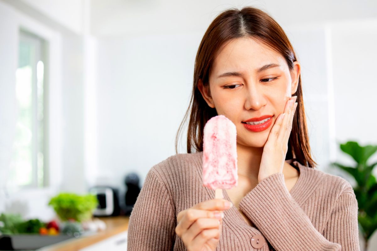 Woman holding pink toothbrush in bright kitchen, smiling at dental care product.