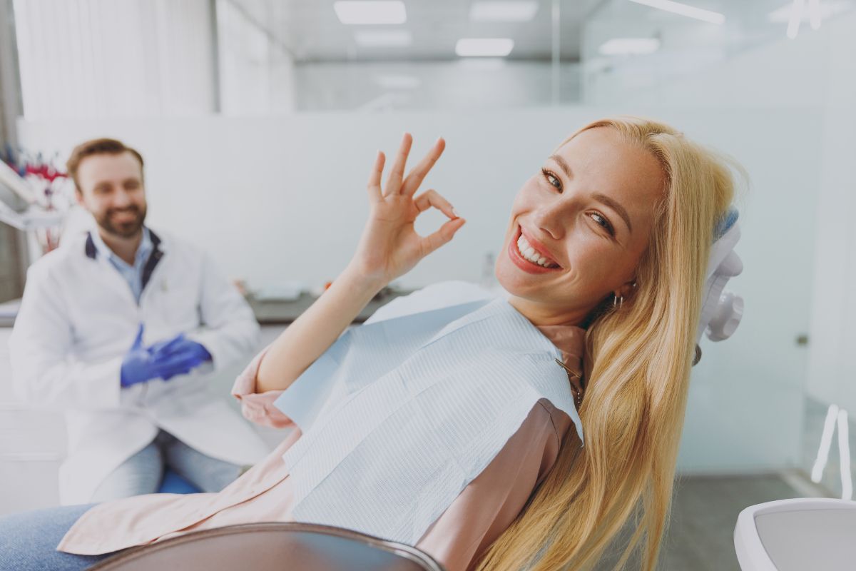 Happy patient in dental chair giving thumbs up during checkup with dentist.