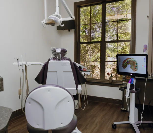 A dental chair with attached instruments, overhead light, and medical equipment in a dental clinic.