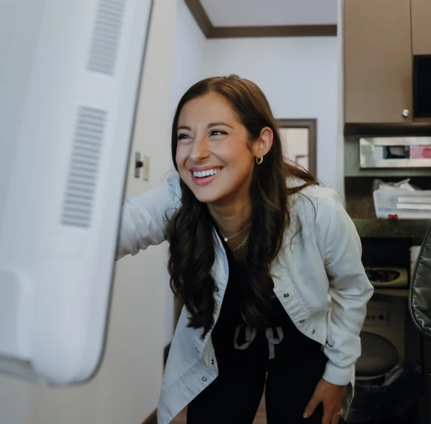 A smiling dentist standing beside dental imaging equipment in a clinic